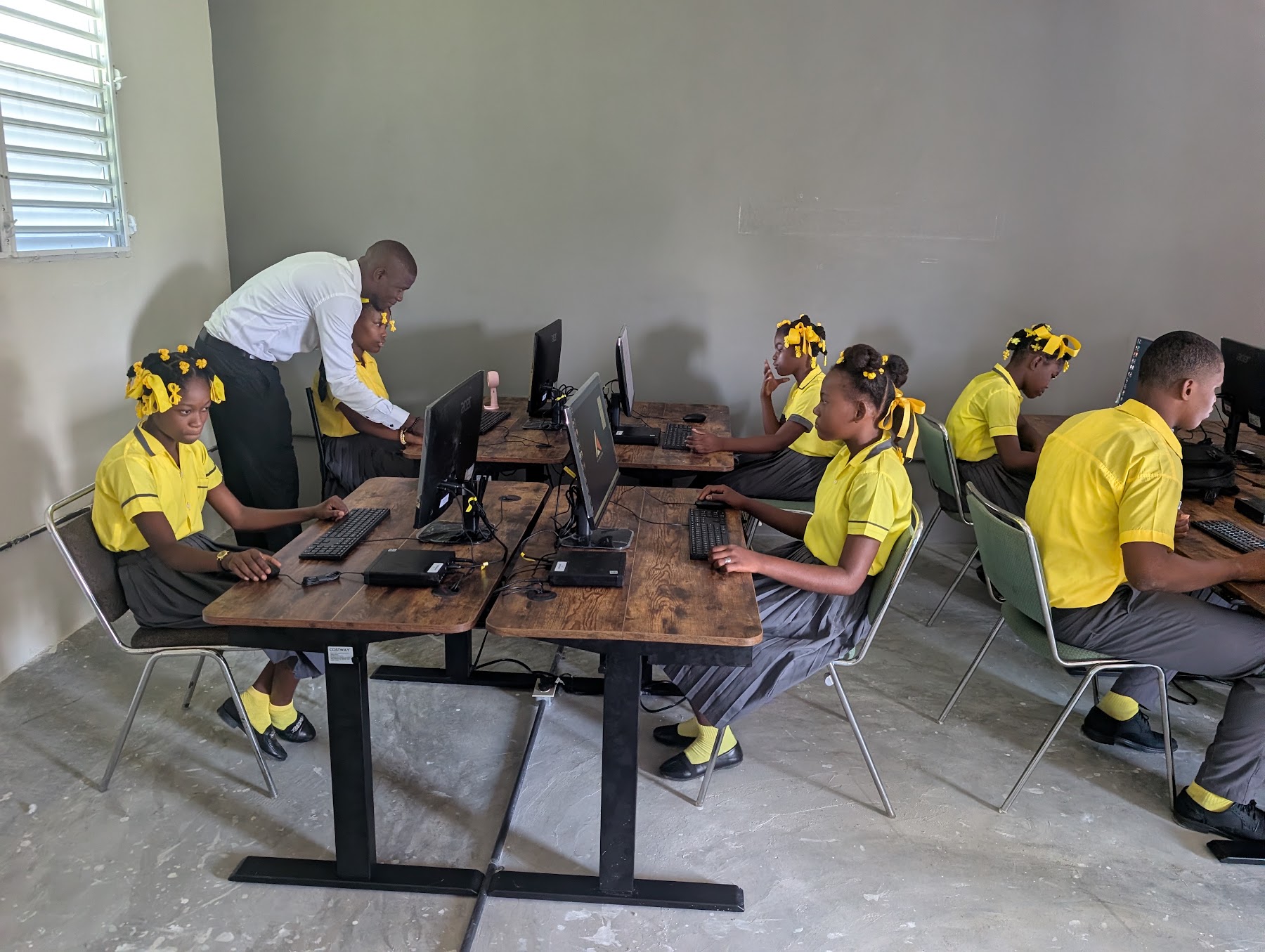 An adult helps a student at a computer while others work nearby